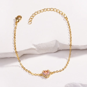 Gros plan d'un bracelet cœur doré avec pierre rose et zircons sur pierre blanche