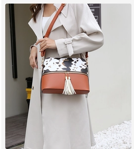 Fashionable cow print crossbody bag with white tassel detail worn by a model in a trench coat