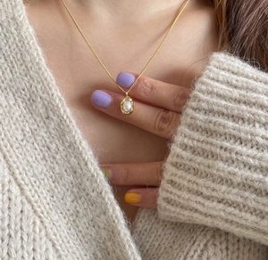 Detail of a gold 925 silver necklace with a pearl pea pod pendant on a model
