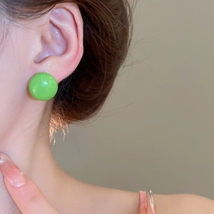 Close-up of bright green round stud earring on earlobe with polished finish