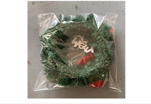 Detail of Christmas wreath with pine needles and Merry signboard in clear packaging