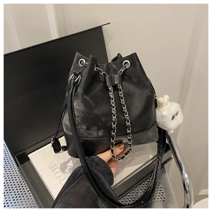 Detail of black bucket bag featuring metal chain strap and a white plush toy charm