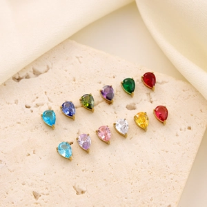 Collection of colorful teardrop zircon pendants in gold metal on a cream silk background