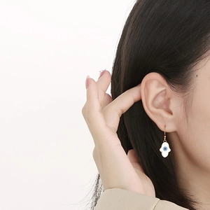 Close-up of golden Hamsa hand earrings with evil eye detail worn by a model
