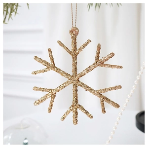 Close-up of a sparkling gold snowflake ornament with sequins hanging from a festive pine branch