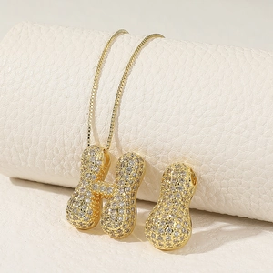 Macro detail of golden box chain with crystal-encrusted bubble H pendant and peanut charm