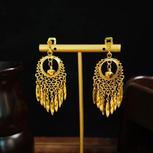 Detail of golden hollow round earrings with long tassel fringe on black background