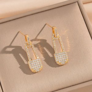 Detailed view of gold safety pin earrings with pave cubic zirconia in a beige box