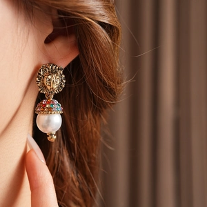 Dettaglio degli orecchini vintage a testa di leone con strass colorati e pendente di perla