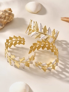 Dettaglio di bracciali a polsino con foglie d'oro e trame su un display di sabbia