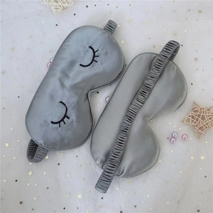 Detail of grey silk eye mask with embroidered eyelashes and elastic strap on starry tulle