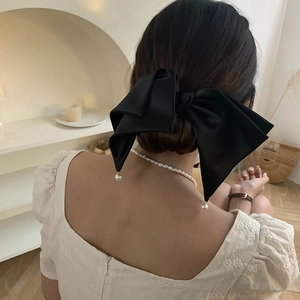 Detail of a large black satin bow hair clip with elegant pearl charms on a model