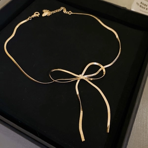Detail of a golden bow knot necklace on a snake chain inside a black velvet jewelry box
