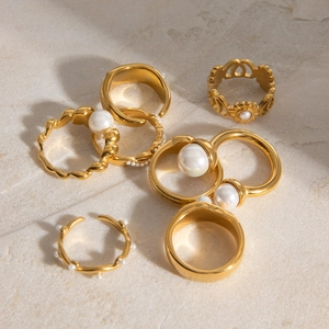 Golden stainless steel rings with pearls and wave textures on stone background