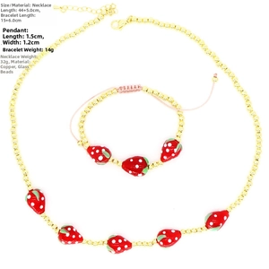 Detailed view of red glass strawberry charms and golden copper beads jewelry set