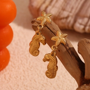 Detailed view of 18K gold-plated starfish and seahorse earrings on rustic wood branch