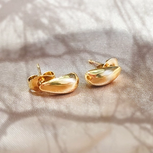 Dettaglio di orecchini a goccia in oro lucido su un elegante tessuto di seta champagne