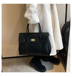 Detail of black leather tote bag with gold metal twist lock closure held by model