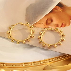 Golden stainless steel hoop earrings with textured beads on a vintage aesthetic background