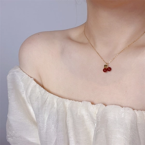 Elegant gold necklace with red cherry pendant worn by model against light background