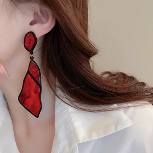 Close-up of geometric red resin earrings with black trim on a model showing artistic style