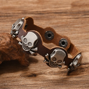 Detail of a brown leather bracelet featuring vintage metal skulls on a rustic wood background