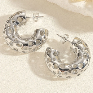Macro detail of silver C-shaped earrings featuring hollow heart patterns on stone surface