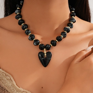 Macro view of black acrylic beads and large heart pendant on a vintage sweater necklace