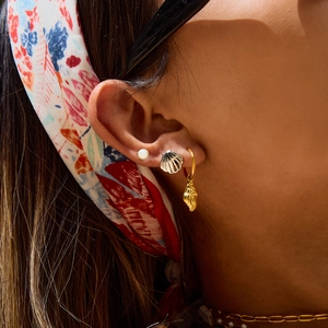 Close-up of pearl studs and seashell earrings worn on ear for a delicate beach style