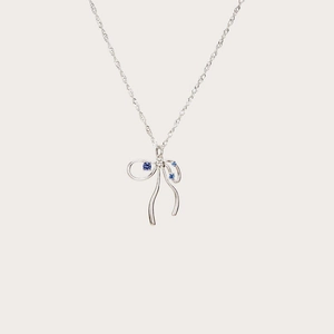 Detail view of silver bow necklace featuring a centered blue zircon gemstone on cream base