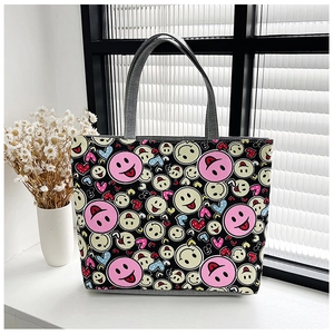 Close-up of black canvas tote bag with colorful smiley face and heart patterns on white table