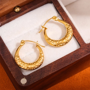 Golden textured hammered hoop earrings with a drop shape on a white jewelry display