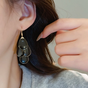 Detail of elegant black and gold teardrop tassel earrings worn by a female model