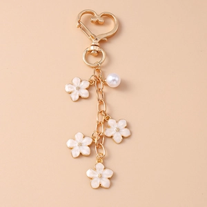 Detailed macro of golden keychain with white enamel flowers, heart clasp and a pearl accent
