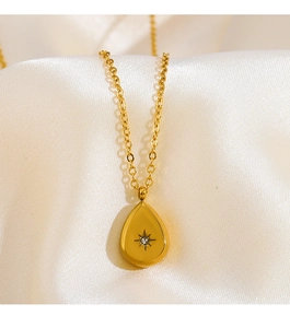 Detail of a gold starburst teardrop pendant on white silk with zircon stone