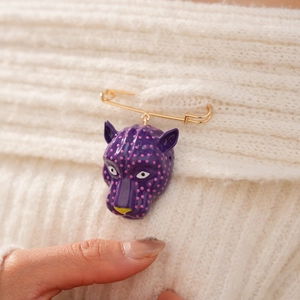 Détail d'une broche tête de léopard violette à pois roses épinglée sur un pull en maille blanc.