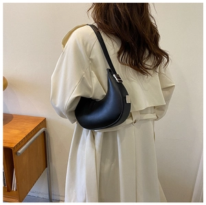 Minimalist black leather half-moon shoulder bag styled on a person with silver hardware