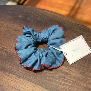 Detail of blue denim scrunchie with red wave stitched edges on a wood background