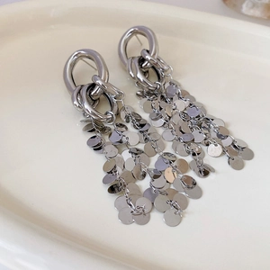 Detailed view of silver tassel earrings with metallic sequins on a ceramic plate