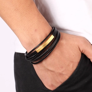 Dettaglio uomo che indossa bracciale in pelle nera intrecciata con placca dorata