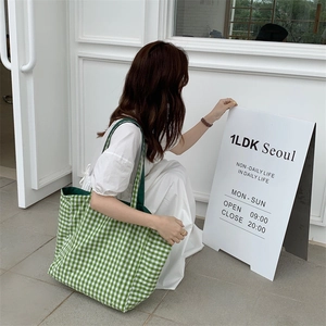 Side view of large green and white checkered canvas tote bag shown in a street style setting