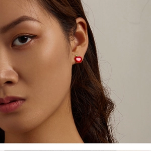 Close-up of a festive red enamel apple stud earring with gold edges on a model's ear