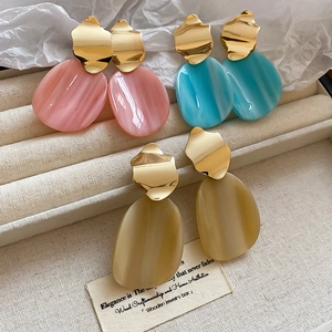 Detail of three pairs of irregular gold earrings with pink, blue, and beige resin pendants