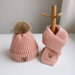 Pink knitted baby hat and scarf set featuring soft brown faux fur pom poms for winter warmth