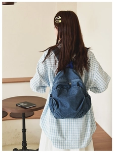 Blue denim backpack shown from behind on model in a minimalist cafe setting