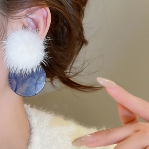 Close-up of winter earrings with white fur balls and blue marble circular pendants