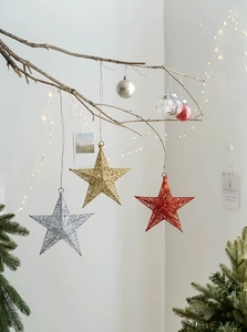 Close-up of glittery red, gold, and silver iron Christmas star ornaments with hanging ropes