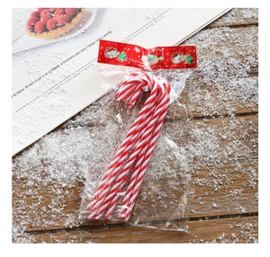 Close-up of six red and white striped Christmas candy cane ornaments on snowy wood background