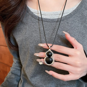 Détail du pendentif en forme de gourde en bois avec perles noires sur cordon noir