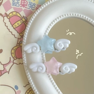 Cute star hair clips with white wings in pastel pink and blue colors on a vintage mirror